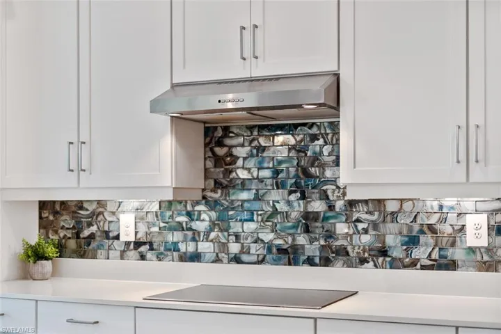 Room details with backsplash, black electric cooktop, white cabinetry, and exhaust hood