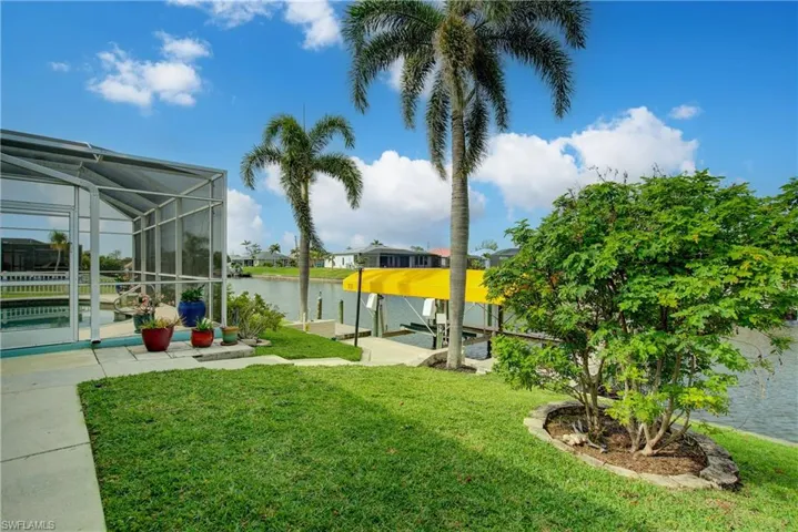 View of yard with glass enclosure, a water view, boat lift, and a dock