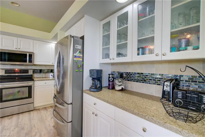 Kitchen featuring light stone counters, stainless steel appliances, white cabinets, light wood-style floors, and decorative backsplash