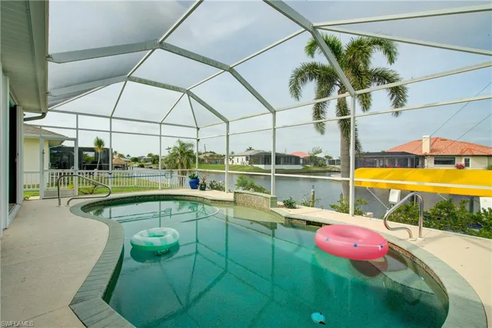 Pool with glass enclosure, a water view, and a patio area