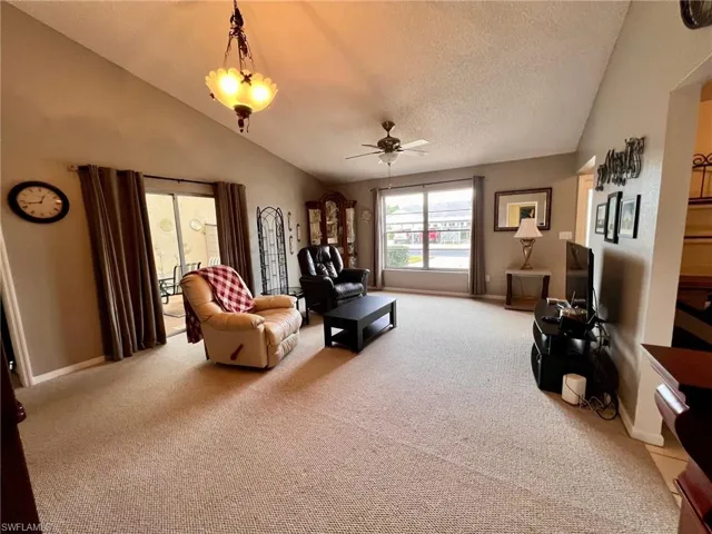 Carpeted living area with vaulted ceiling, a ceiling fan, and a textured ceiling