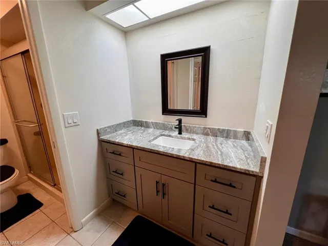 Full bathroom featuring vanity, a textured wall, a stall shower, and light tile patterned floors