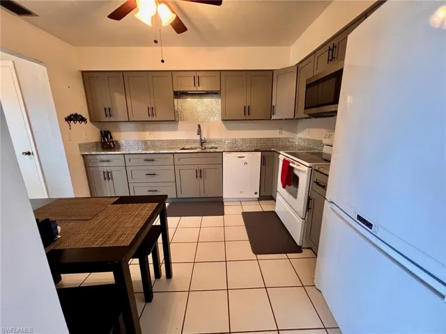 Kitchen with white appliances, gray cabinetry, light tile patterned floors, a ceiling fan, and light stone countertops