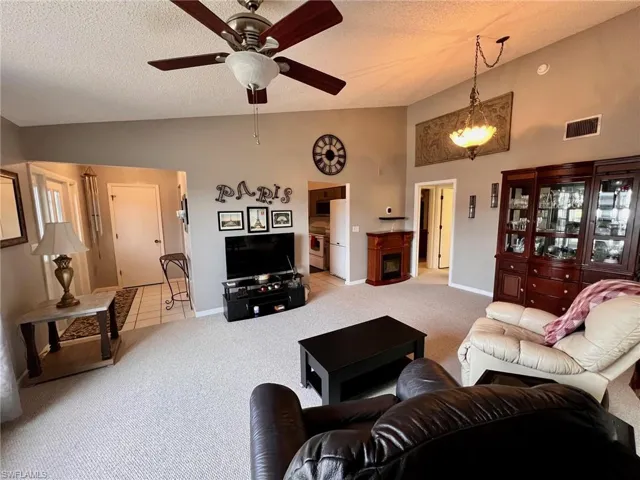 Living area featuring a textured ceiling, carpet floors, ceiling fan, and high vaulted ceiling