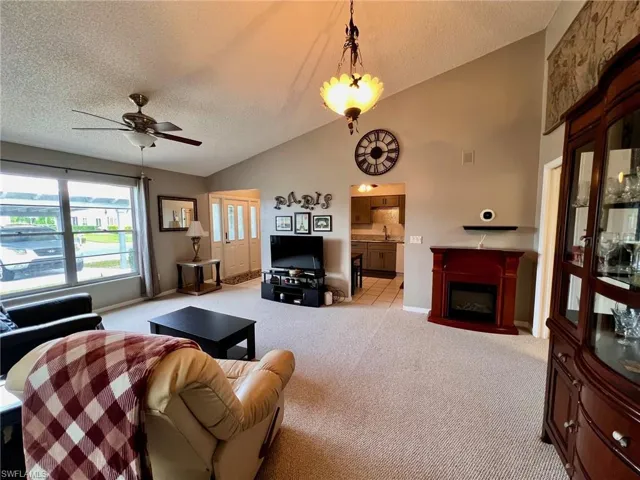 Living room with a textured ceiling, lofted ceiling, light carpet, a fireplace, and ceiling fan
