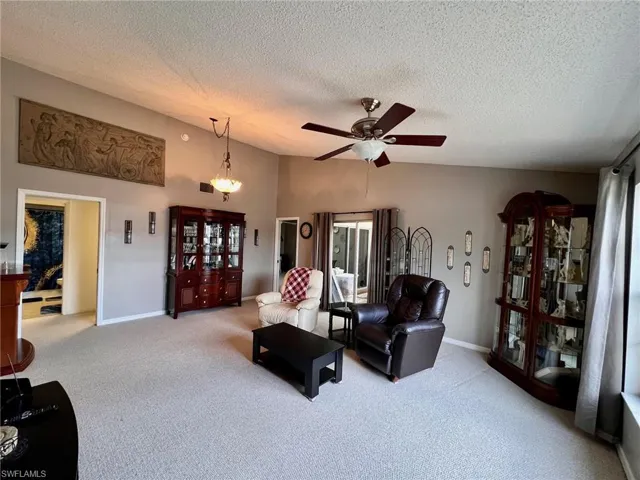 Carpeted living room with vaulted ceiling, a textured ceiling, and a ceiling fan