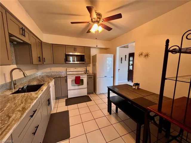 Kitchen with light stone counters, white appliances, gray cabinets, ceiling fan, and light tile patterned floors