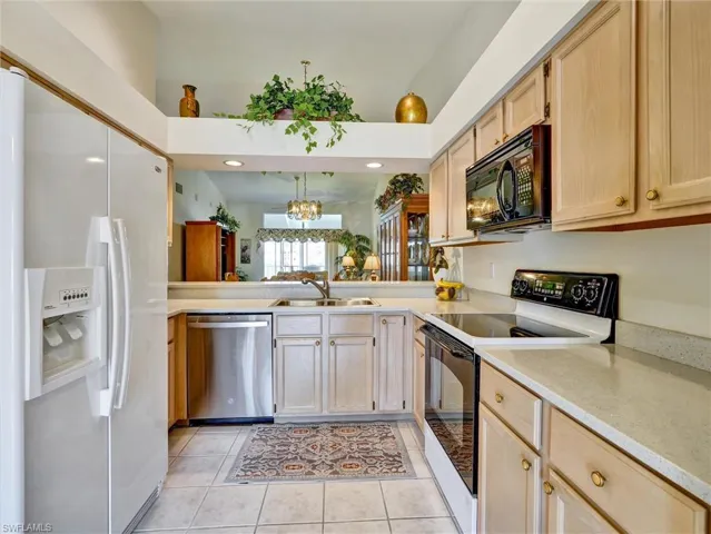 Kitchen featuring white appliances, light brown cabinetry, light tile patterned flooring, and light stone countertops