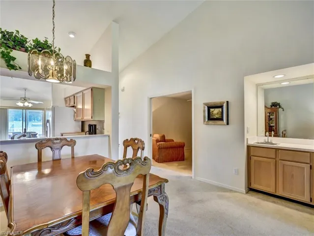 Dining room featuring a chandelier, light colored carpet, high vaulted ceiling, a ceiling fan, and recessed lighting