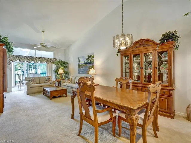 Dining area featuring light carpet, high vaulted ceiling, a chandelier, and ceiling fan