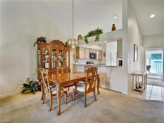 Dining room featuring light colored carpet, high vaulted ceiling, and a chandelier