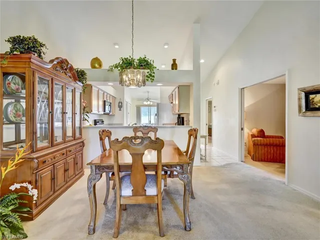 Dining room featuring high vaulted ceiling, a chandelier, light carpet, and light tile patterned flooring