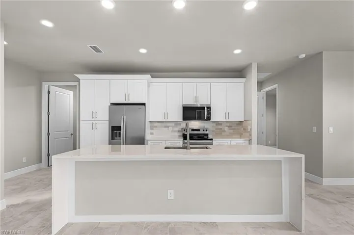 Kitchen with light stone counters, stainless steel appliances, white cabinets, a spacious island, and recessed lighting