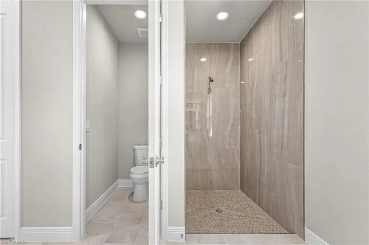 Full bathroom with a tile shower, recessed lighting, and a textured wall