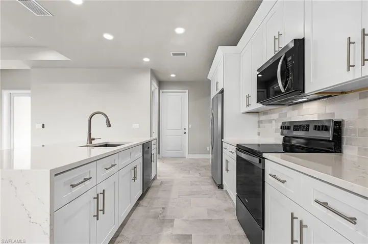 Kitchen featuring appliances with stainless steel finishes, white cabinetry, recessed lighting, light stone counters, and backsplash
