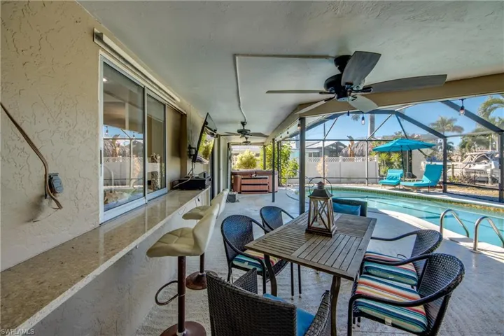 View of patio featuring glass enclosure, a ceiling fan, a sunroom, a hot tub, and outdoor dining space