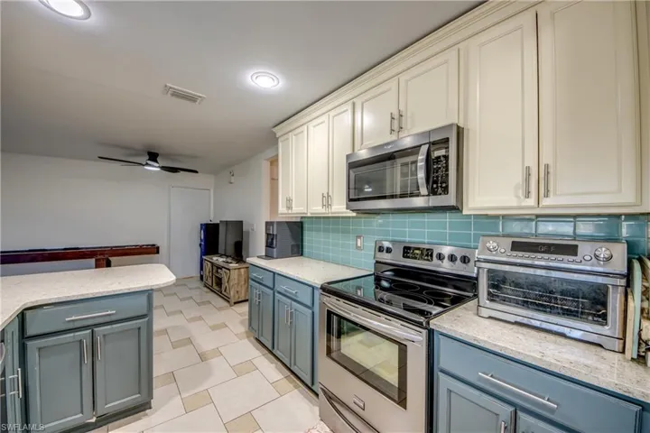Kitchen with stainless steel appliances, light stone counters, decorative backsplash, and a ceiling fan