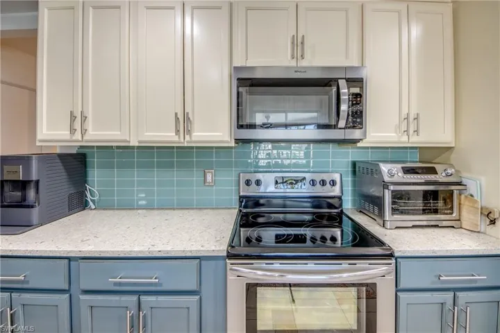 Kitchen with stainless steel appliances, light stone countertops, backsplash, and white cabinetry