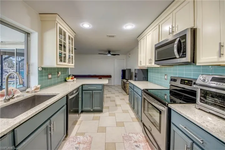 Kitchen with stainless steel appliances, light stone counters, glass insert cabinets, a peninsula, and recessed lighting