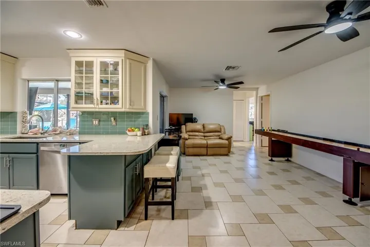 Kitchen with glass insert cabinets, a breakfast bar area, stainless steel dishwasher, open floor plan, and light stone counters