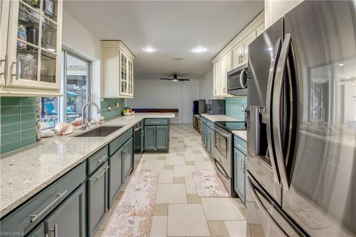 Kitchen featuring stainless steel appliances, light stone counters, a peninsula, backsplash, and glass insert cabinets