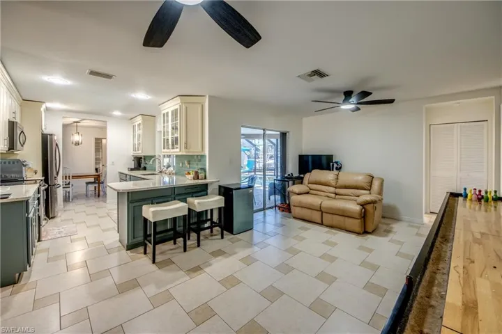 Kitchen with glass insert cabinets, light stone countertops, a kitchen bar, green cabinetry, and open floor plan