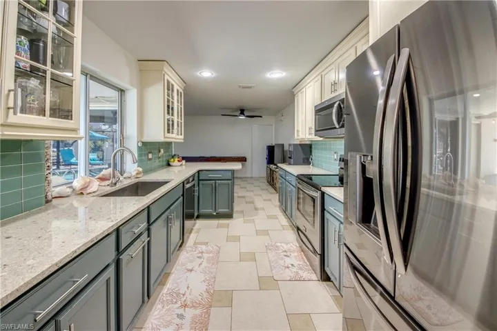 Kitchen with stainless steel appliances, light stone counters, glass insert cabinets, white cabinetry, and recessed lighting