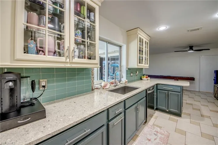 Kitchen with light stone counters, glass insert cabinets, a peninsula, a ceiling fan, and recessed lighting