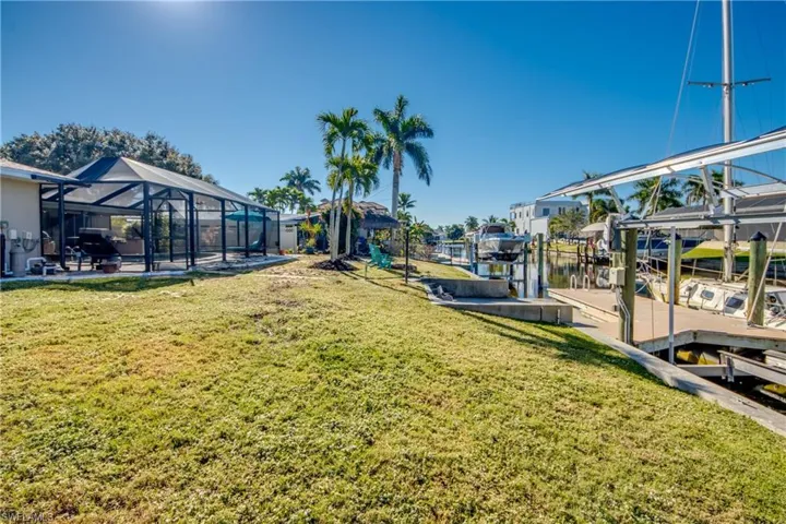 View of green lawn with boat lift, a sunroom, a boat dock, glass enclosure, and a water view