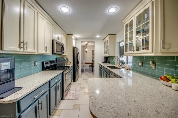 Kitchen with stainless steel appliances, light stone countertops, glass insert cabinets, white cabinetry, and backsplash