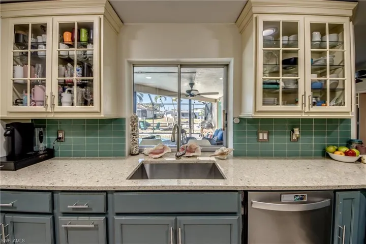 Kitchen featuring glass insert cabinets, light stone countertops, dishwasher, and cream cabinets
