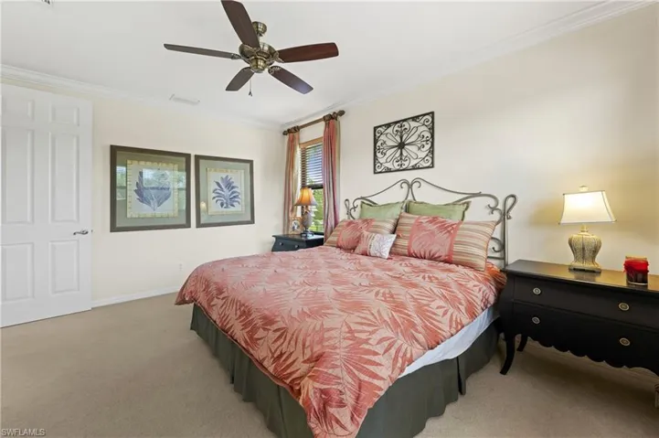 Carpeted bedroom featuring a ceiling fan with integrated lighting, crown molding, a paneled door, and window with blinds and drapes