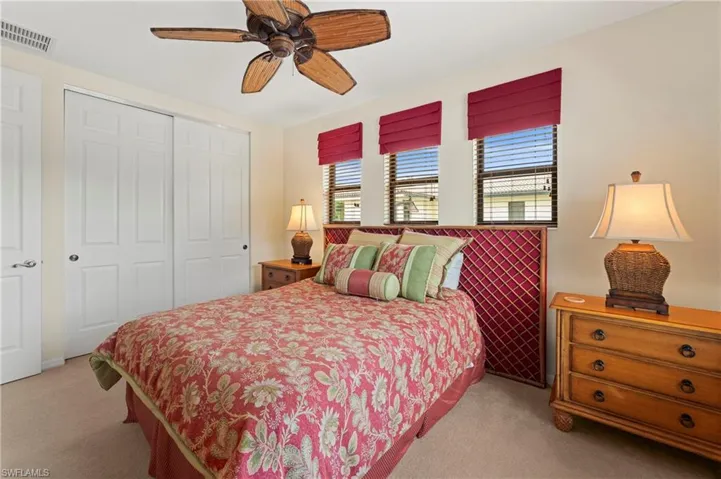 Carpeted room featuring a ceiling fan with wood-finish blades, a six-panel bi-fold closet, three windows with blinds and red roman shades, and a textured headboard