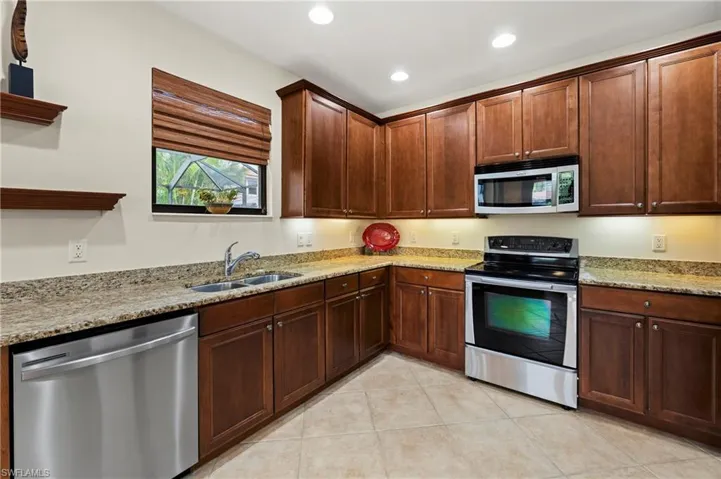 Kitchen featuring wood cabinetry, stainless steel appliances, speckled stone countertops, and tile flooring