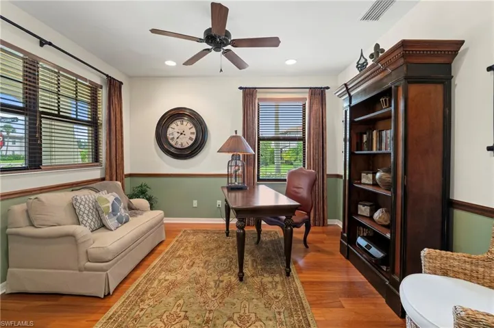 Room featuring wood-finish flooring, two windows with blinds and drapes, a ceiling fan with integrated lighting, recessed lighting, and built-in shelving
