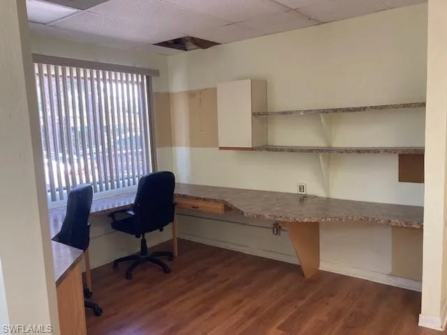 Office space with a drop ceiling, dark wood-type flooring, plenty of natural light, and built in study area