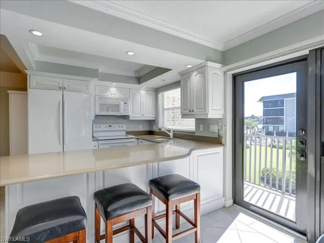 Kitchen featuring white appliances, a breakfast bar area, white cabinetry, crown molding, and recessed lighting