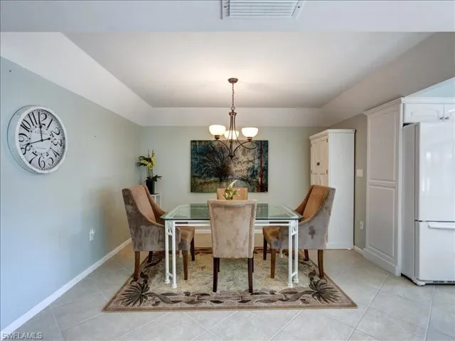 Dining space with light tile patterned flooring, a chandelier, and a raised ceiling