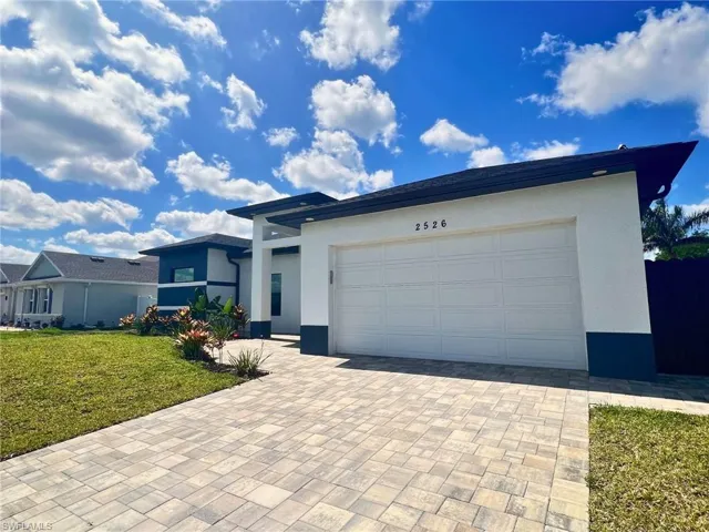 View of front of property featuring stucco siding, decorative driveway, a front lawn, and an attached garage