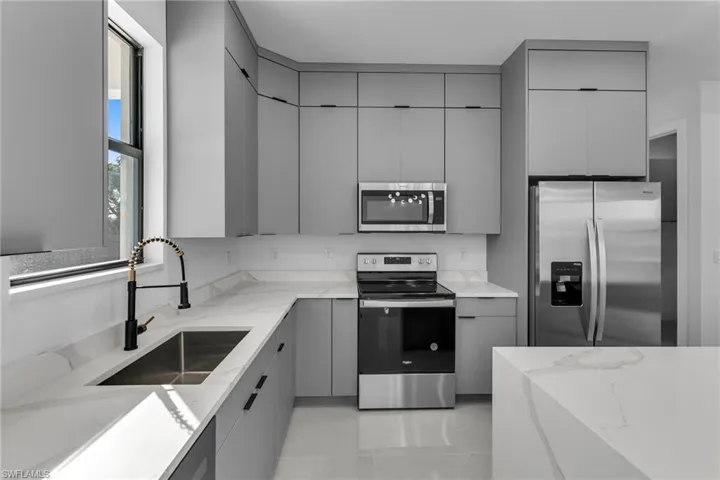 Kitchen with stainless steel appliances, gray cabinetry, a sink, and light stone countertops