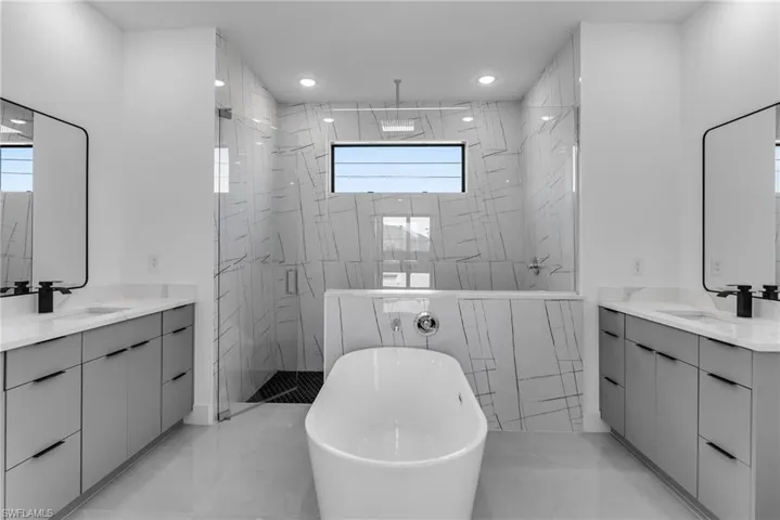 Full bath with a marble finish shower, two vanities, healthy amount of natural light, and recessed lighting