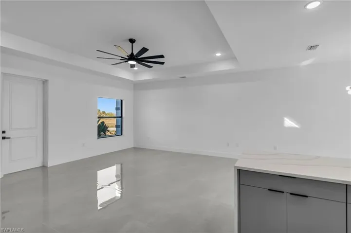 Empty room with a tray ceiling, recessed lighting, a ceiling fan, and baseboards