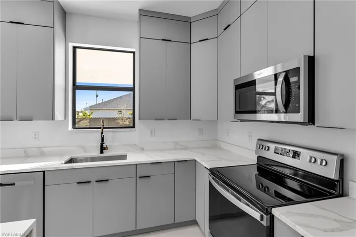 Kitchen featuring stainless steel appliances, gray cabinets, a sink, and light stone counters