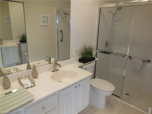 Bathroom featuring a shower with shower door, oversized vanity, toilet, and tile floors