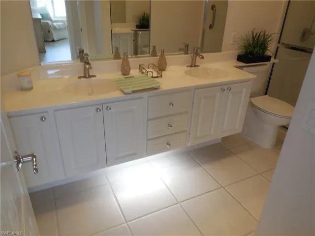 Bathroom featuring double sink vanity, tile flooring, and toilet