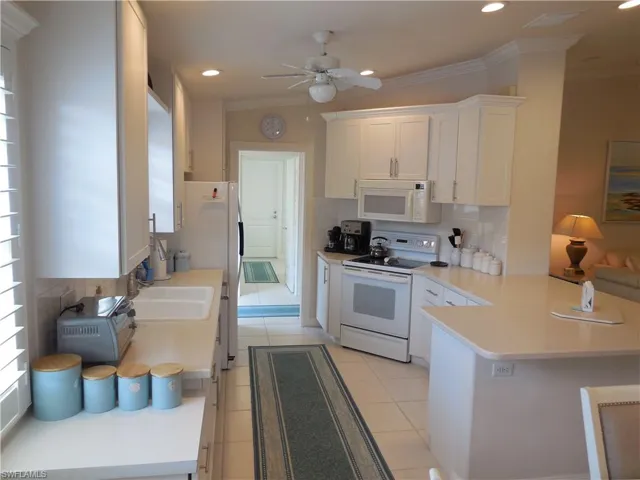 Kitchen with white appliances, white cabinets, kitchen peninsula, backsplash, and ceiling fan