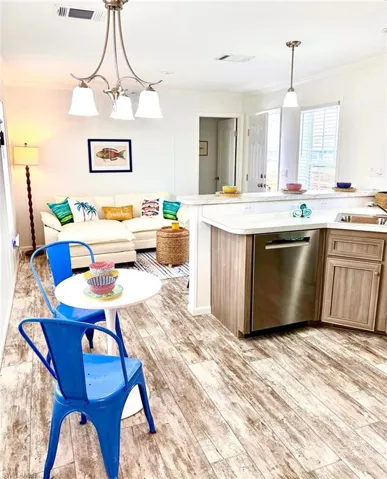 Kitchen with light countertops, stainless steel dishwasher, light wood-type flooring, ornamental molding, and open floor plan