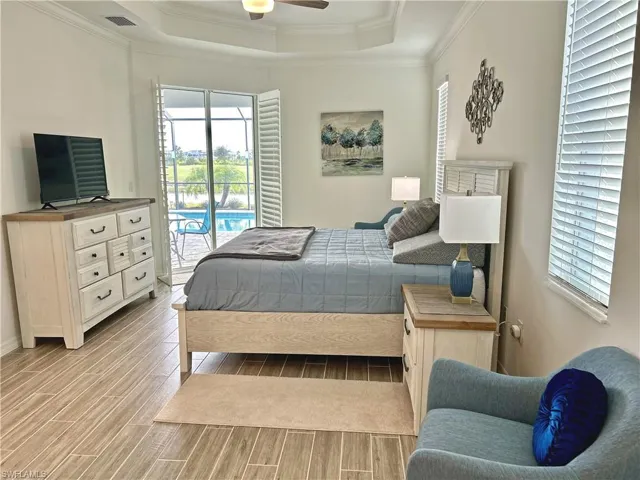 Bedroom with access to exterior, light wood-type flooring, a tray ceiling, and multiple windows