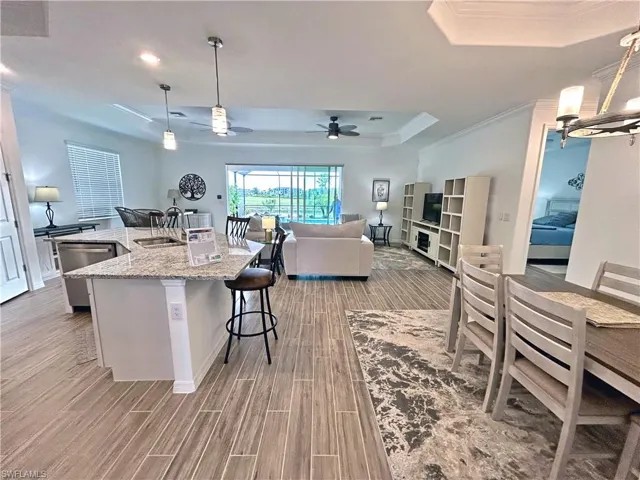 Kitchen featuring hanging light fixtures, light stone counters, light hardwood / wood-style floors, a center island with sink, and ceiling fan with notable chandelier