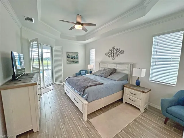Bedroom with a raised ceiling, multiple windows, ceiling fan, and light hardwood / wood-style floors